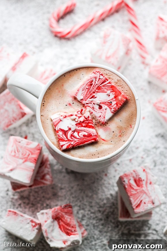 Candy Cane Cloud Bites 4 A close-up of a square of homemade Peppermint Marshmallow, showcasing its fluffy texture and a hint of the red swirl, resting on a bed of powdered sugar.