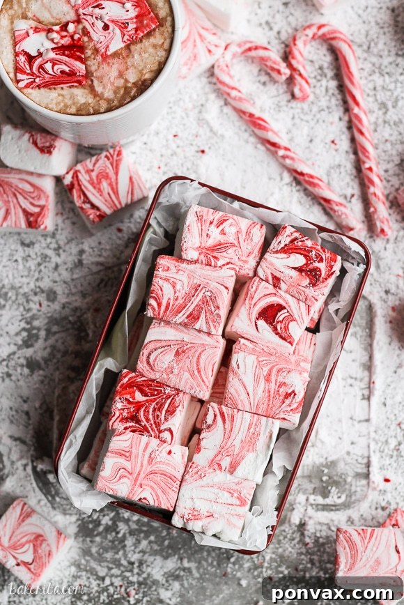 Candy Cane Cloud Bites 5 An array of homemade Peppermint Marshmallows with red swirls, some cut into squares, others into festive shapes, piled elegantly for presentation.