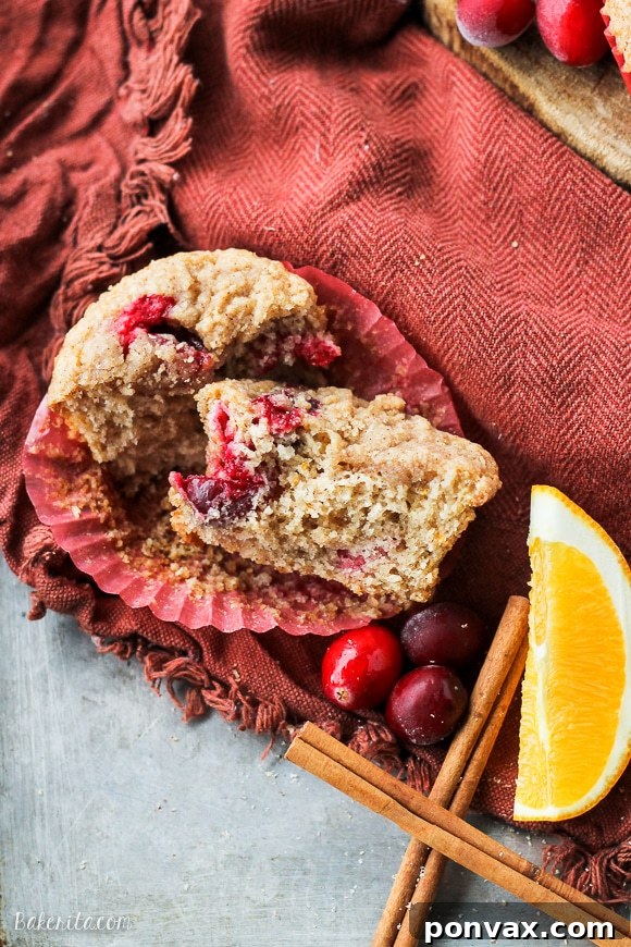 A stack of freshly baked Vegan Cranberry Orange Muffins with a golden-brown streusel topping.