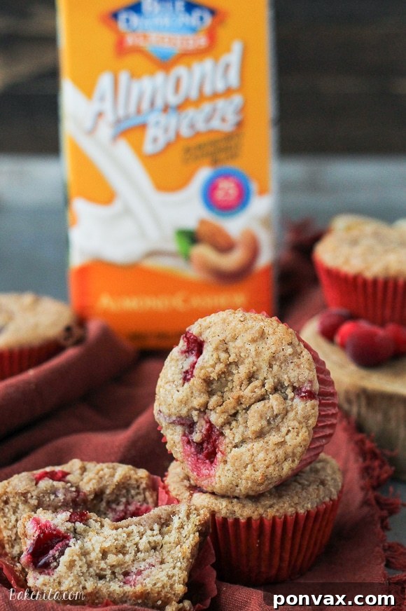 A close-up of a single Vegan Cranberry Orange Muffin, showing its moist interior, cranberries, and streusel.