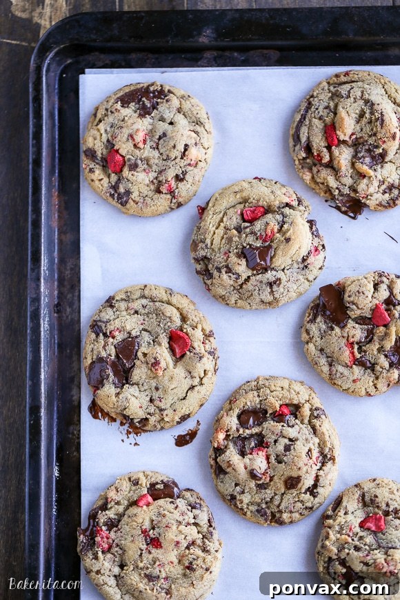 Strawberry Chocolate Indulgence Cookies 6 A close-up shot of several chocolate-dipped strawberry chocolate chip cookies on parchment paper.