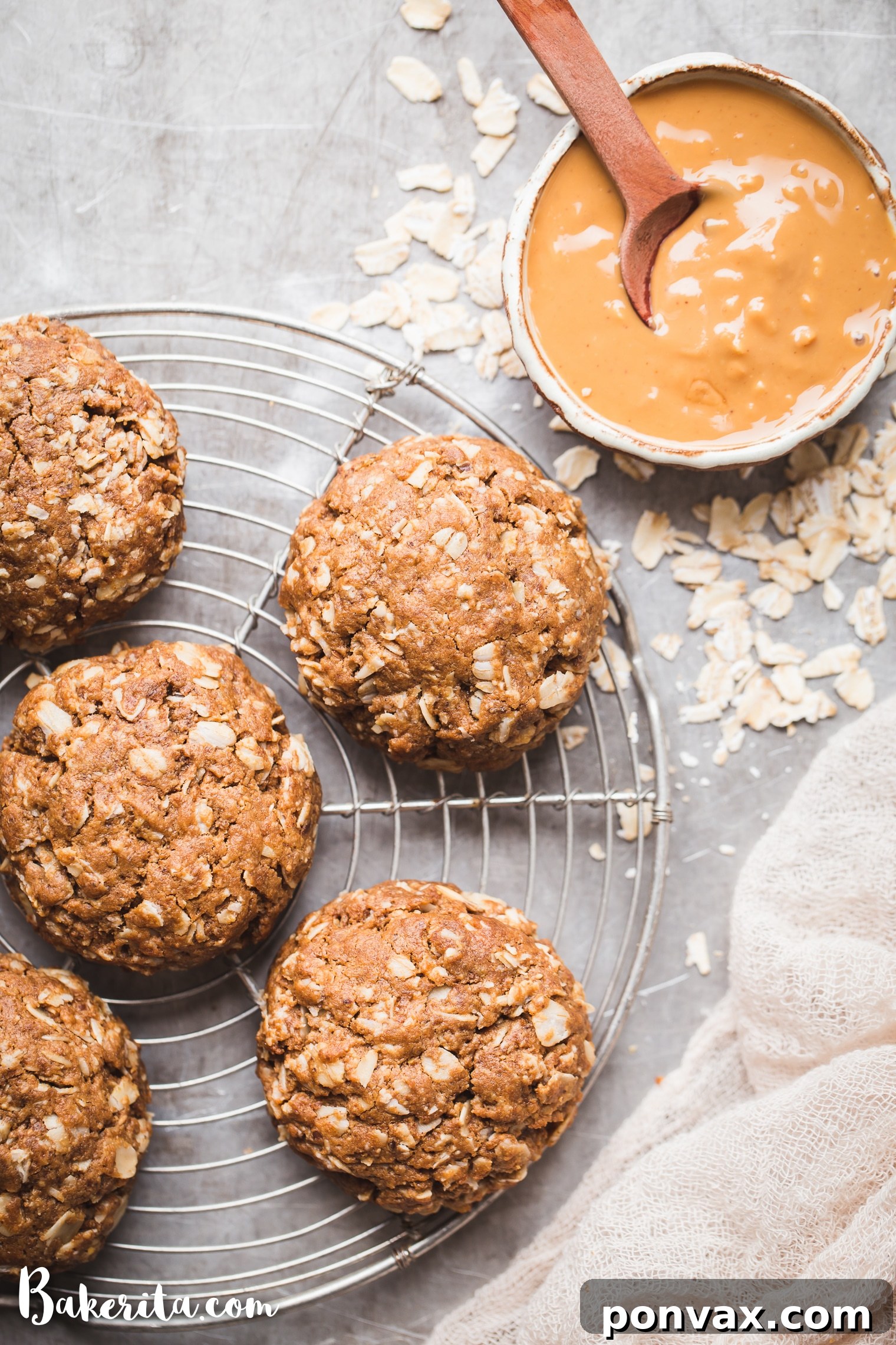 A close-up shot of a single perfectly baked Peanut Butter Oatmeal Cookie, showcasing its soft, chewy texture and golden-brown edges. A small bowl of creamy natural peanut butter sits slightly out of focus in the corner, hinting at the cookie's rich flavor.