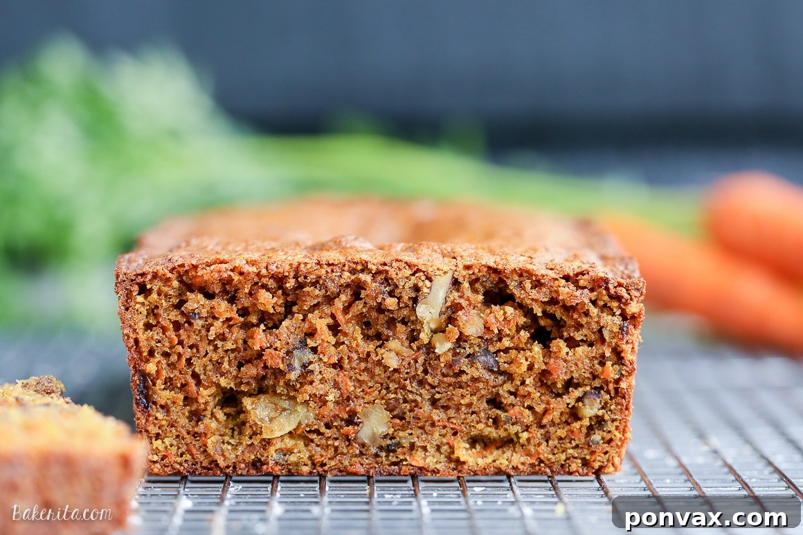 A close-up shot of a slice of moist Paleo Carrot Bread, revealing its rich, spicy interior, studded with walnuts and golden raisins. This gluten-free and dairy-free bread is a healthy indulgence.