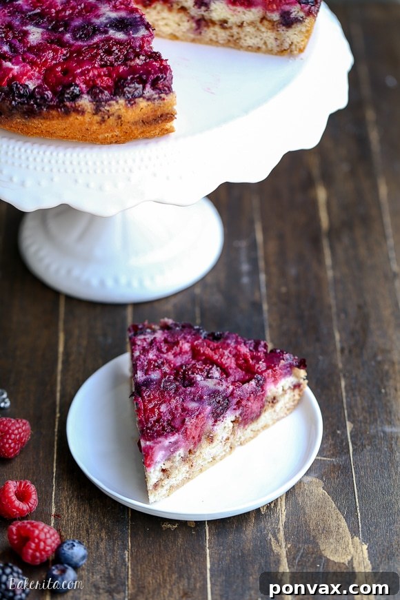 A slice of Berry Upside Down Cake on a white plate, revealing the distinct layers of colorful berries, moist cake, and a rich cinnamon crumb swirl in the middle.