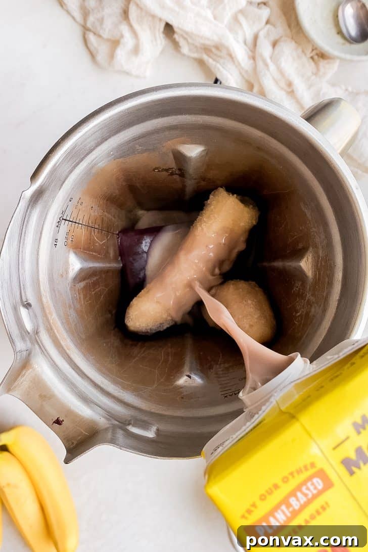 The acai bowl mixture being poured from the blender into a serving bowl, showcasing its thick consistency.