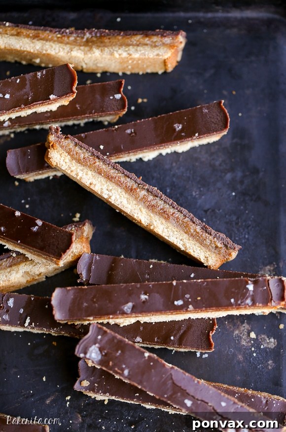 Close-up of a stack of homemade Paleo Twix bars with a bite taken out of one, revealing the cookie, caramel, and chocolate layers.