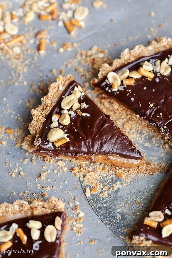 A slice of Chocolate Peanut Butter Tart being lifted, showing the layers of pretzel crust, peanut butter caramel, and chocolate ganache. The dessert is gluten-free and vegan.