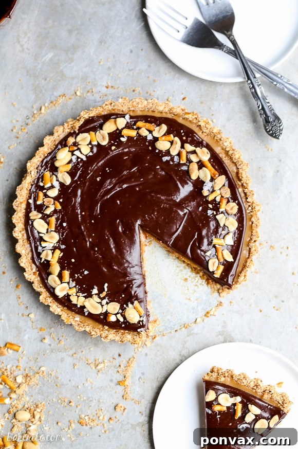 A full Chocolate Peanut Butter Tart, beautifully garnished and ready to be served. It features a pretzel crust, peanut butter filling, and chocolate ganache.