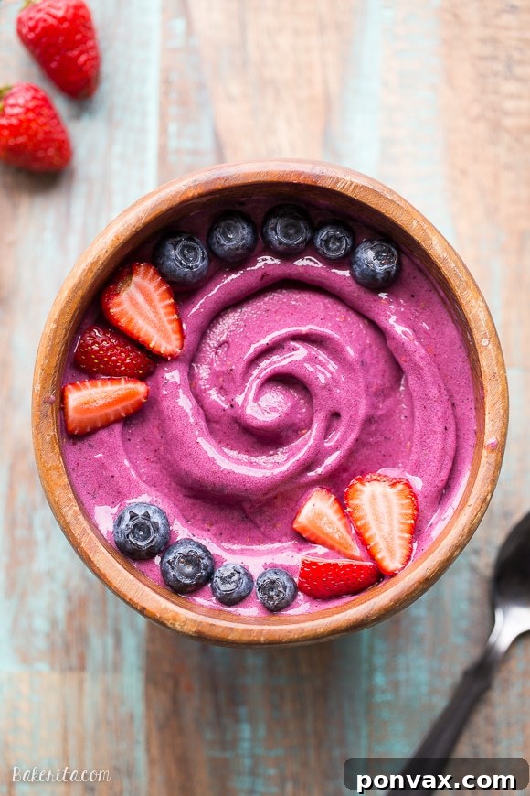 Bowl of Berry Pitaya Smoothie topped with fresh fruit and granola, ready to be eaten.