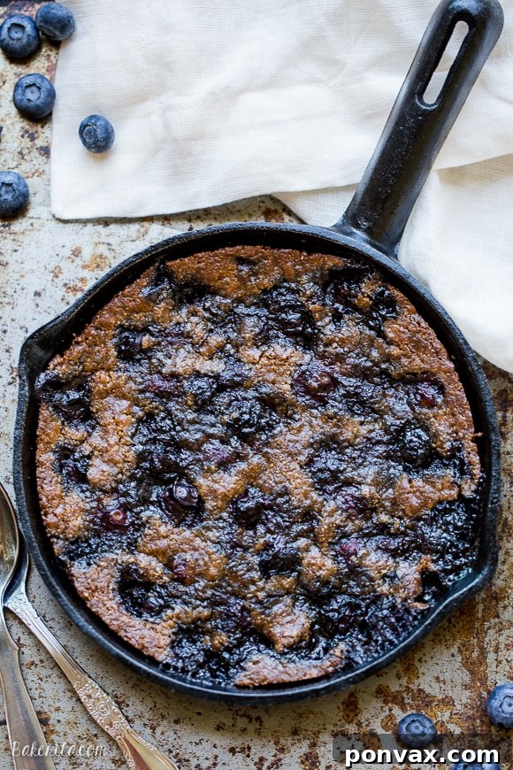 Close-up of the gooey center of a Blueberry Skillet Cookie, showing tender cookie dough dotted with bursting blueberries, served fresh from the skillet.