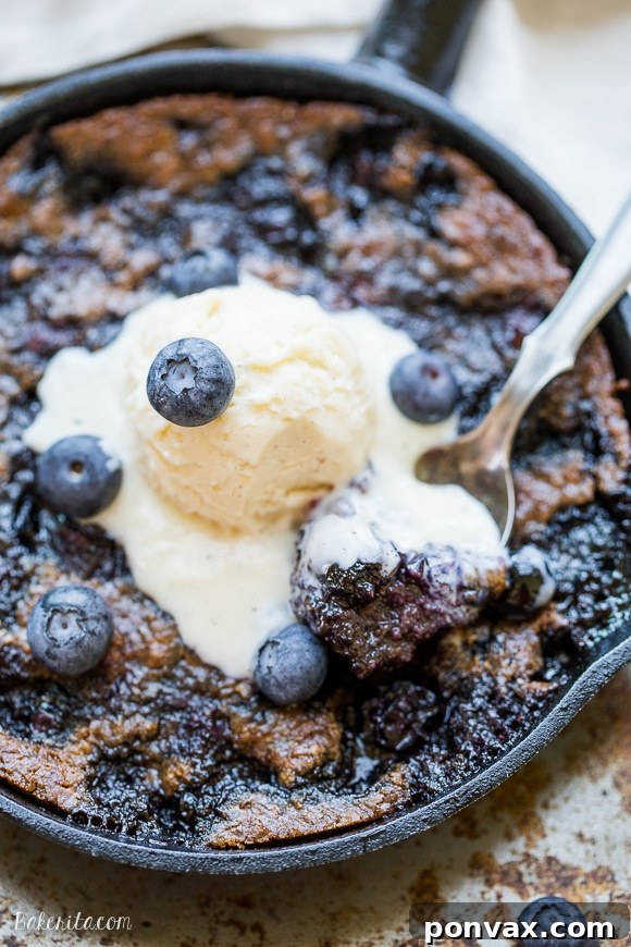 A freshly baked Blueberry Skillet Cookie in a cast iron pan, showing its golden-brown, slightly crisp edges and soft, fruity center, ready to be served.