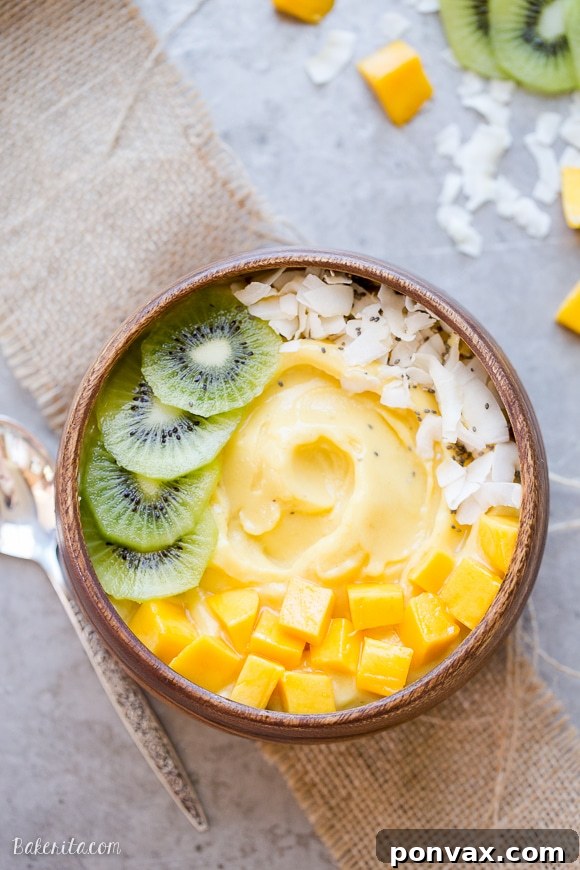 Tropical Mango Pineapple Smoothie Bowl 2 A beautifully arranged Mango Pineapple Smoothie Bowl topped with fresh kiwi slices, juicy mango chunks, shredded coconut flakes, and chia seeds, presented in a rustic wooden bowl.