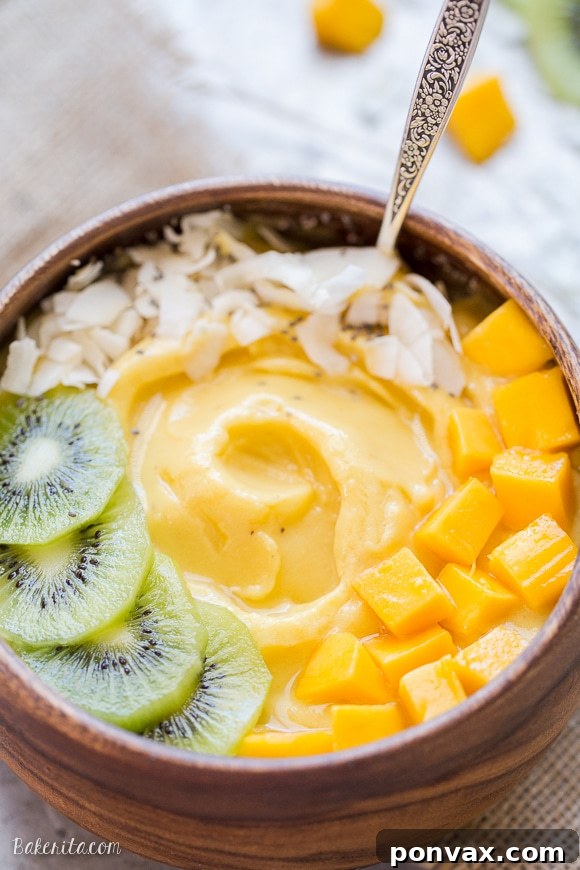 Tropical Mango Pineapple Smoothie Bowl 3 A close-up shot of a Pineapple Mango Smoothie Bowl in a wooden bowl, richly garnished with kiwi slices, fresh mango pieces, coconut flakes, and a sprinkle of chia seeds, highlighting its vibrant colors and textures.