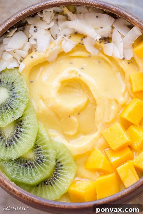 Tropical Mango Pineapple Smoothie Bowl 5 A vibrant close-up of a Mango Pineapple Smoothie Bowl, featuring a generous sprinkle of coconut flakes, artfully arranged kiwi slices on the left, and luscious mango chunks on the right, all in a wooden bowl.