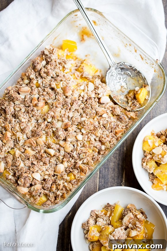 Close-up of the golden, bubbly mango pineapple crumble filling peeking through the coconut macadamia topping in a rustic baking dish, ready to be enjoyed as a tropical delight.