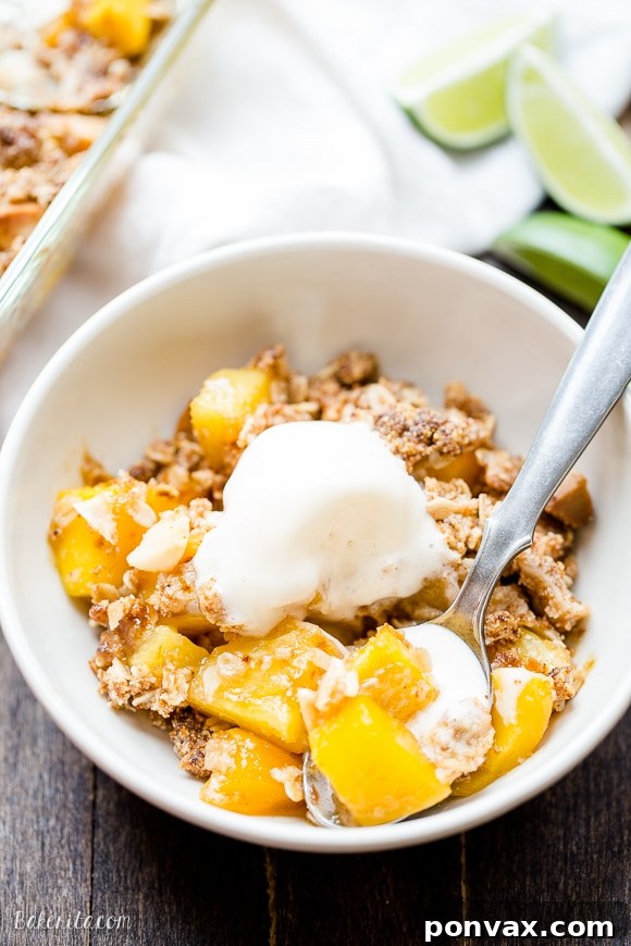 A serving of warm Mango Pineapple Crumble topped with a scoop of dairy-free vanilla ice cream or whipped coconut cream, garnished with fresh mint, highlighting its dessert potential.