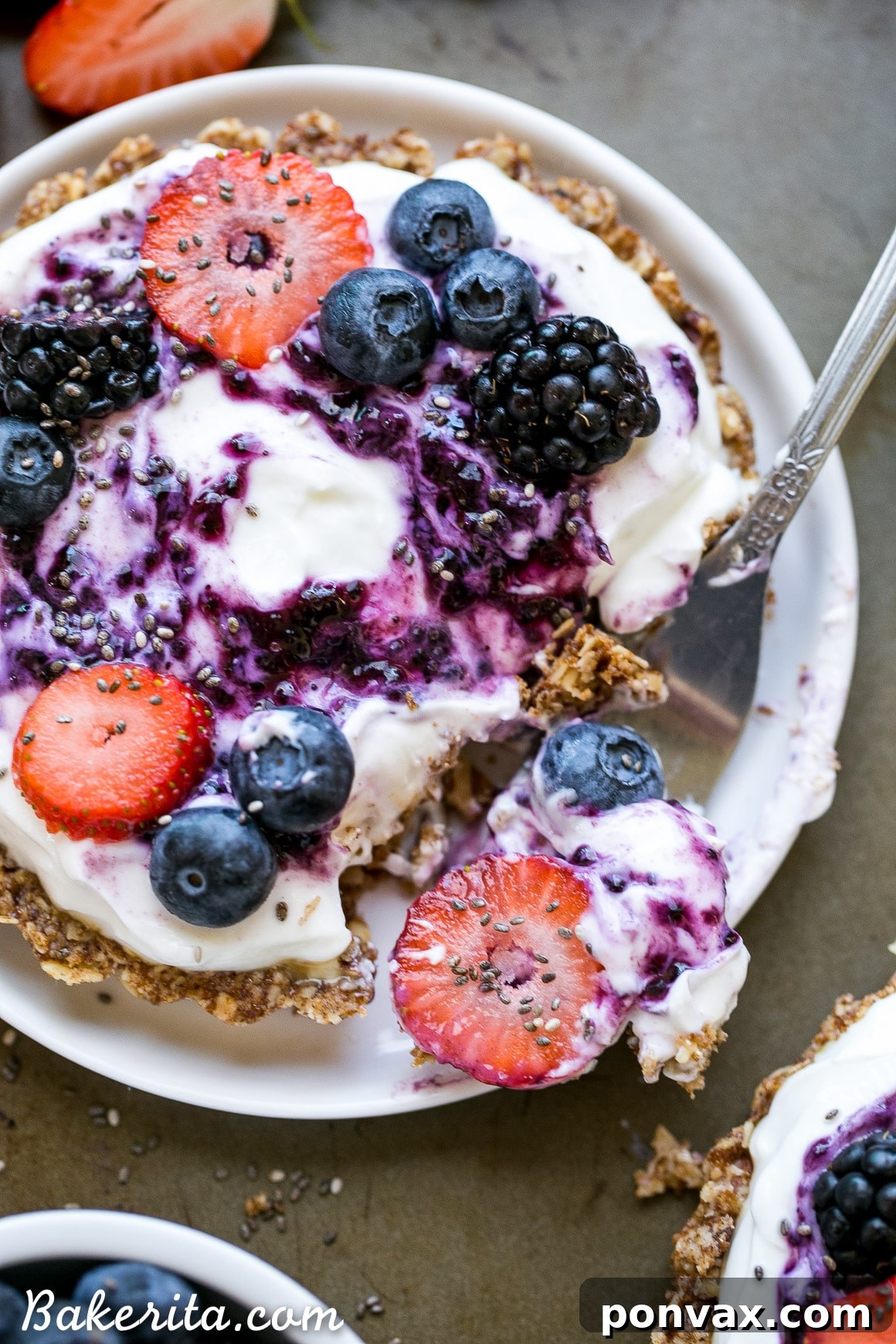 A close-up of the Granola Crust Breakfast Tart being assembled, with a spoon adding creamy Greek yogurt to the crisp granola shell.