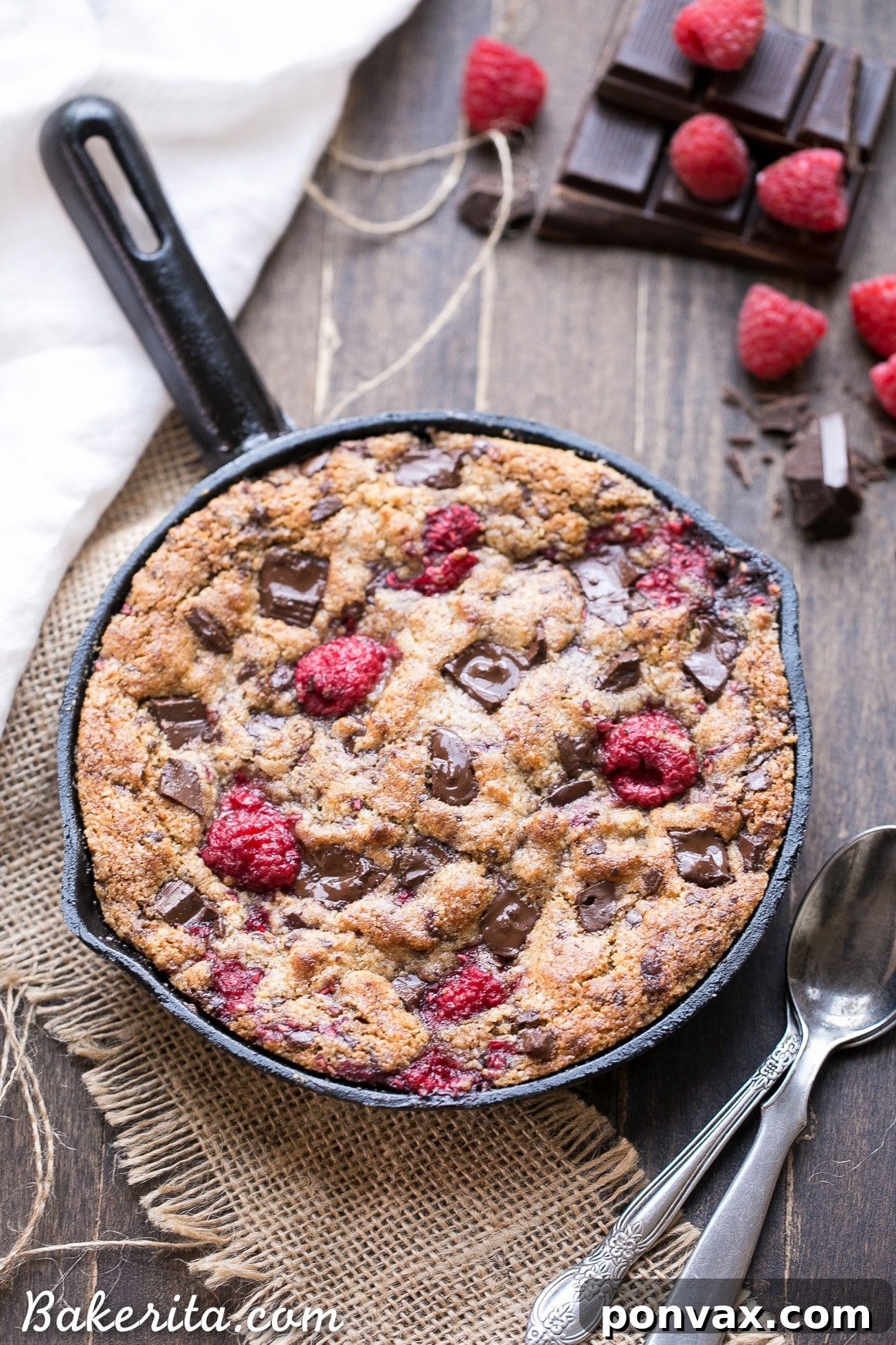 A perfectly baked Raspberry Chocolate Chunk Skillet Cookie, loaded with melted dark chocolate and fresh raspberries, ready to be served warm from the cast iron pan.