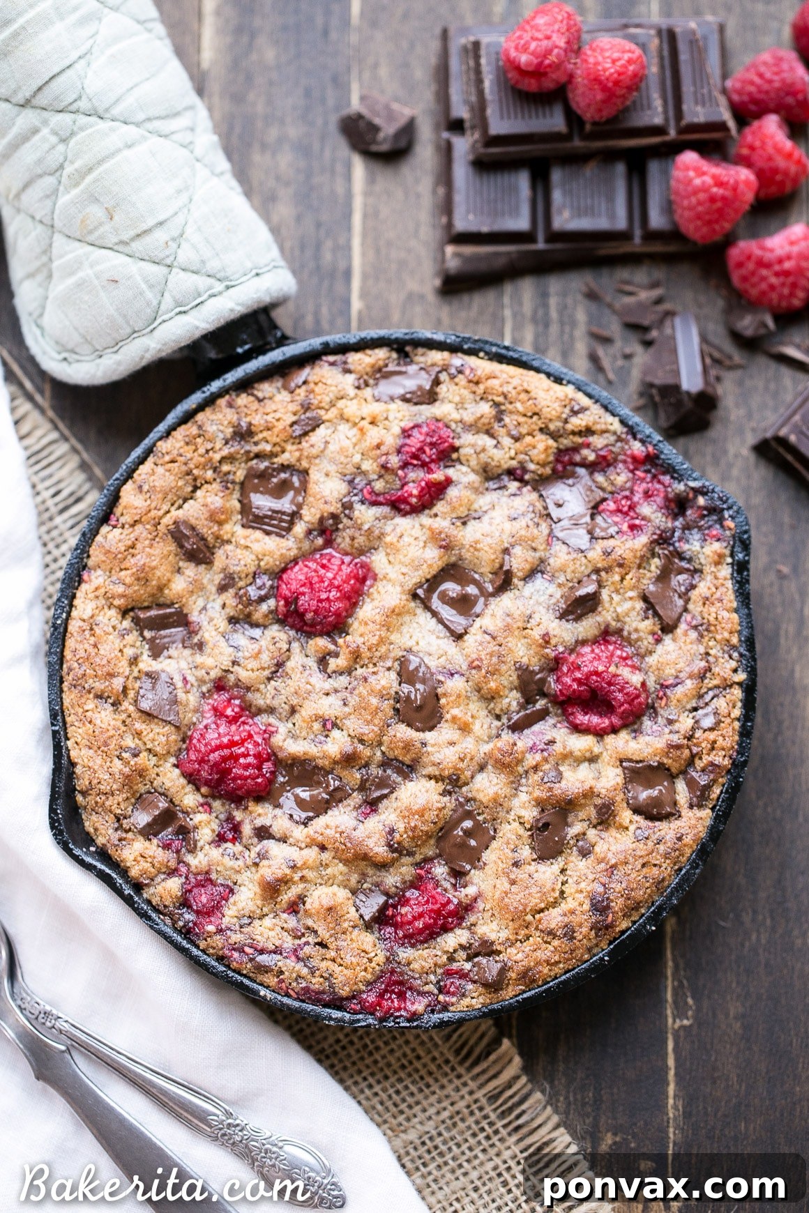 Close-up of a warm Raspberry Chocolate Chunk Skillet Cookie with melted dark chocolate oozing out, highlighting its rich, gooey texture.
