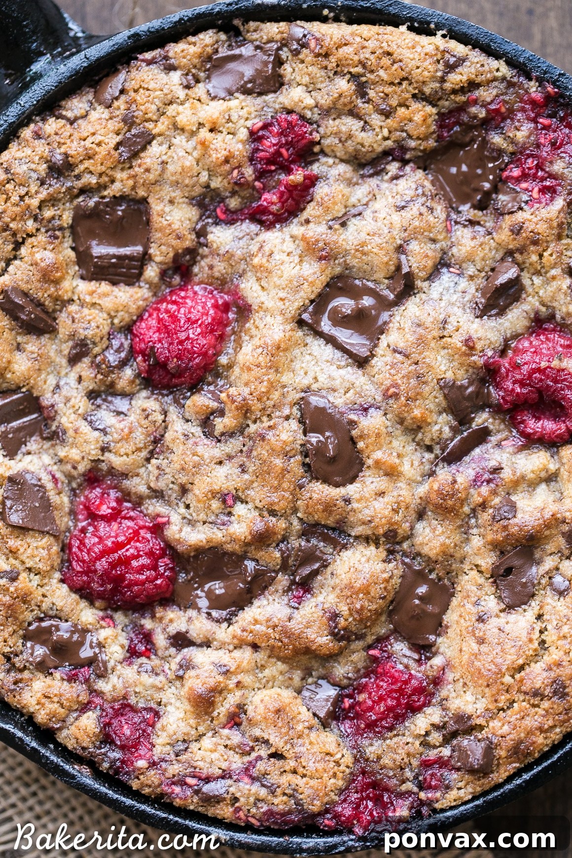 A slice of warm Raspberry Chocolate Chunk Skillet Cookie showcasing the generous chunks of dark chocolate and bright red raspberries.