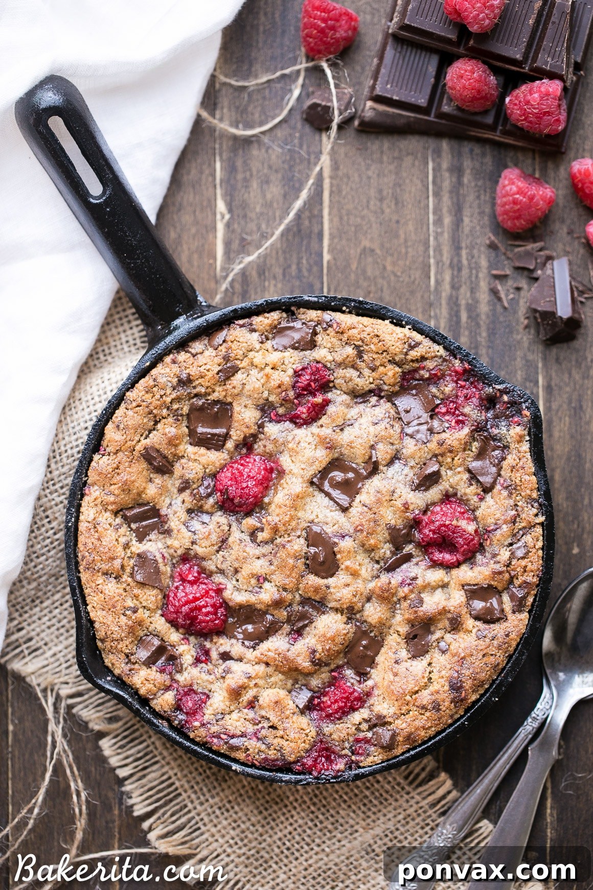 A side view of the Skillet Cookie, showing its thick, soft interior and crispy edges, garnished with fresh raspberries.