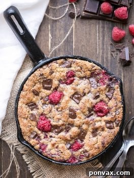 A close-up image of the baked Chocolate Chunk Raspberry Skillet Cookie in a cast iron pan, ready to be enjoyed.