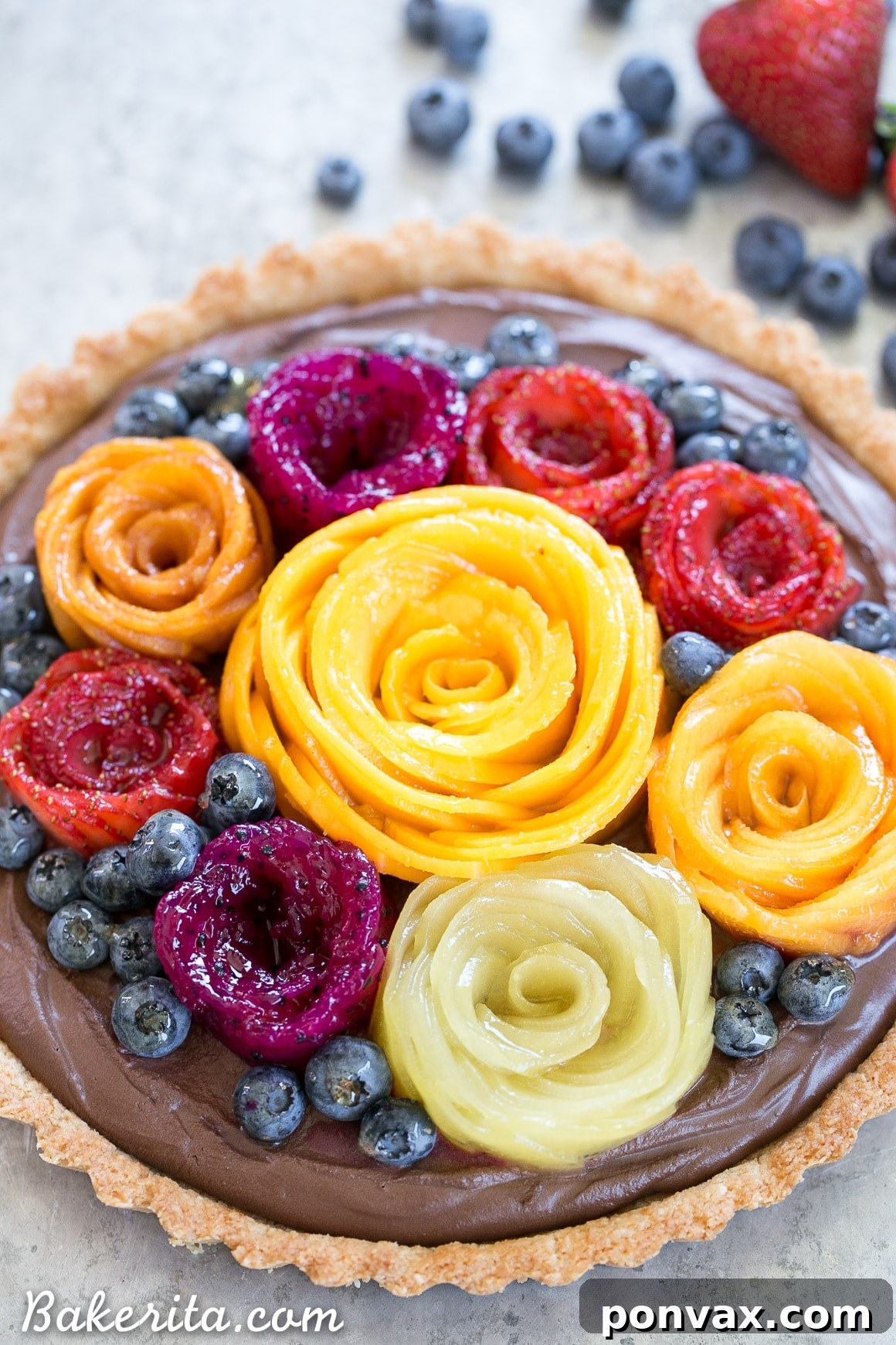 A whole Vegan Chocolate Mousse Tart showcased with its vibrant Fresh Fruit Flowers. The tart features a sturdy Coconut Crust, rich chocolate mousse, and artfully cut mango and strawberry toppings.