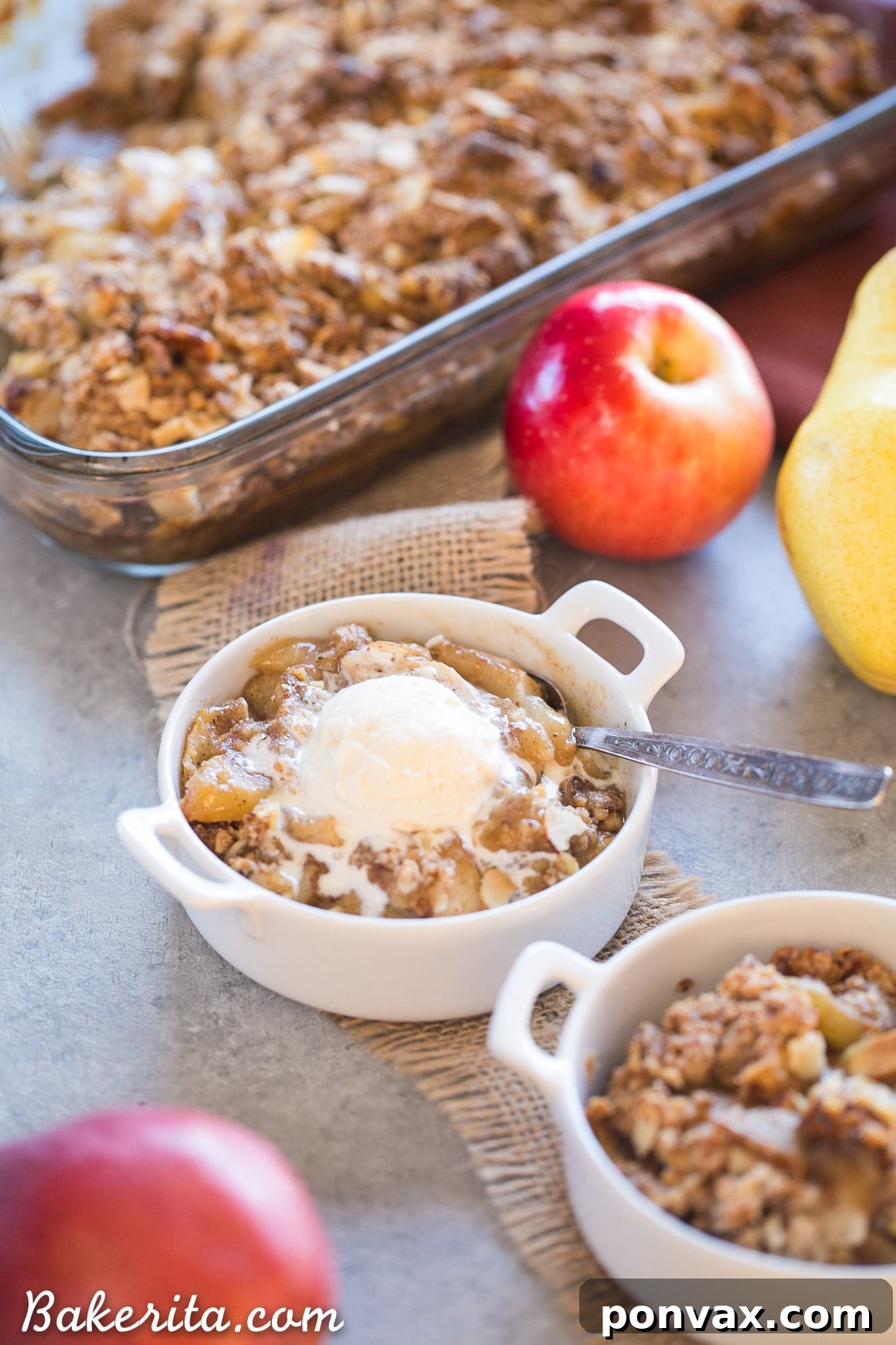 A generous serving of Apple Pear Crisp, freshly baked and still warm, with a scoop of vanilla ice cream melting delicately on top. The textures of the fruit and the crispy topping are clearly visible, promising a truly satisfying gluten-free, Paleo, and vegan treat.