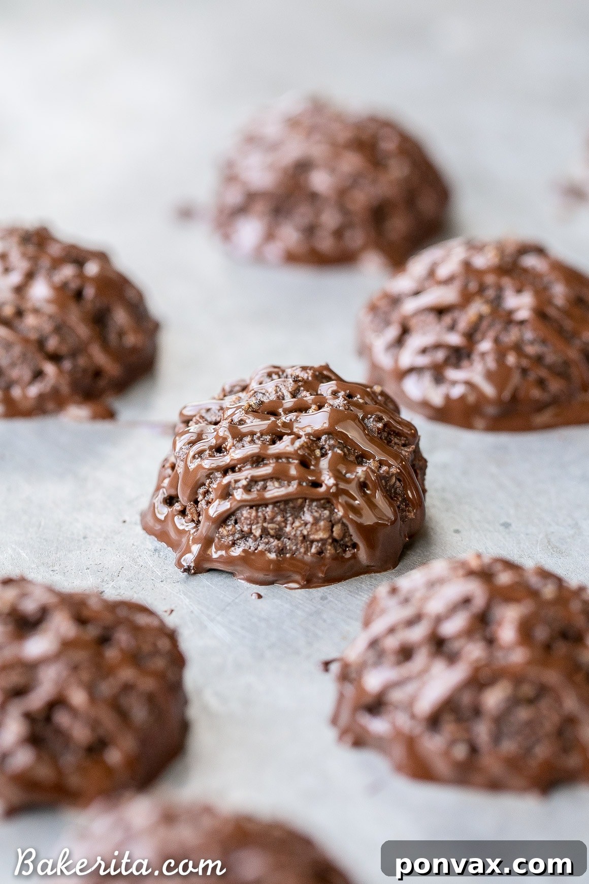 Hand holding a rich Double Chocolate Macaroon, showcasing its texture and the melted chocolate coating, highlighting its gluten-free and vegan nature.