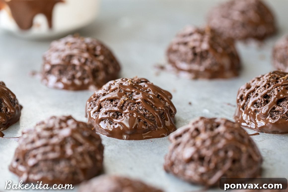 Several freshly baked Double Chocolate Macaroons on parchment paper, waiting for their chocolate dip, emphasizing their fudgy texture.