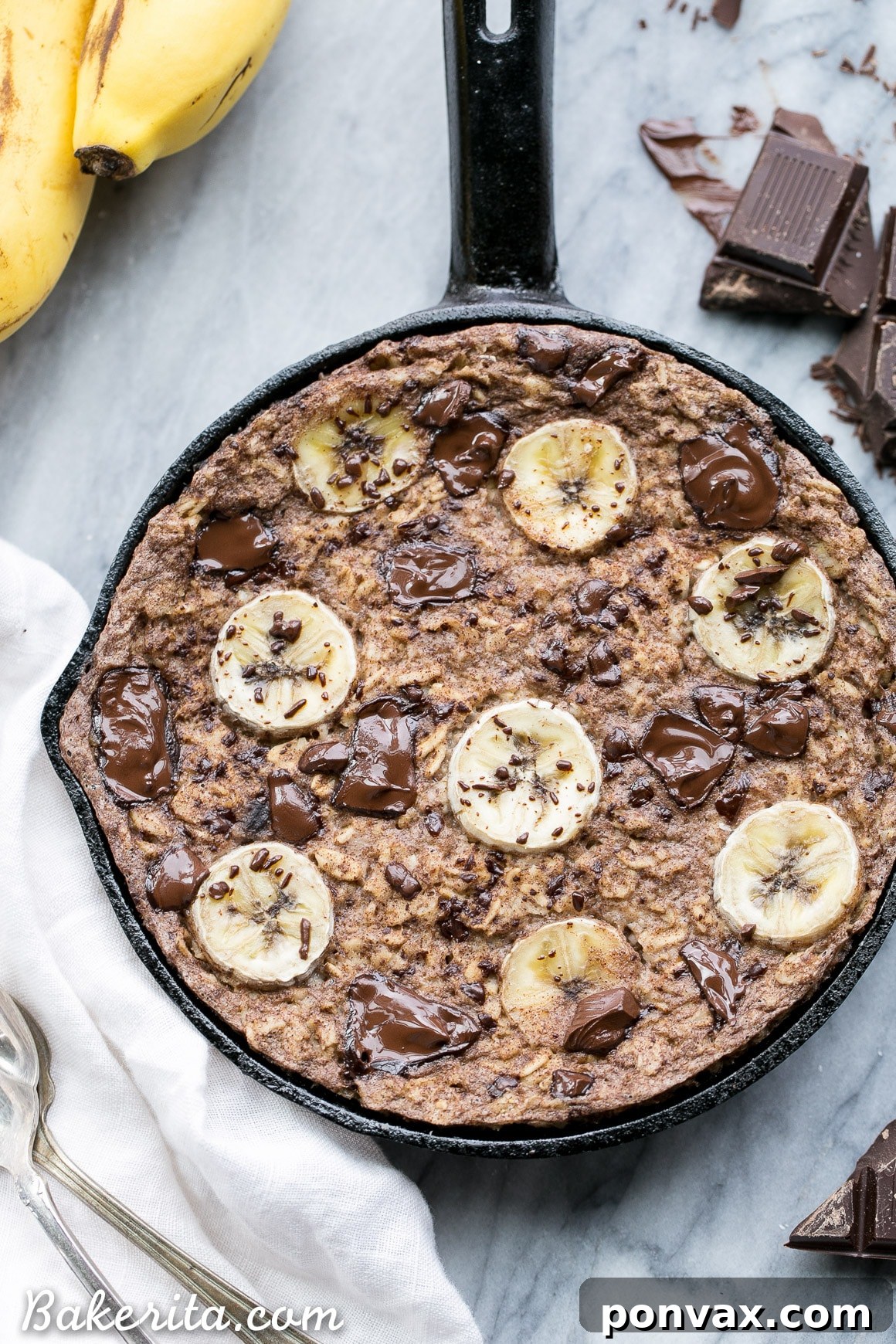 A rustic-looking pan of Chocolate Chunk Banana Baked Oatmeal, topped with fresh banana slices and melted chocolate, ready to be served and enjoyed.