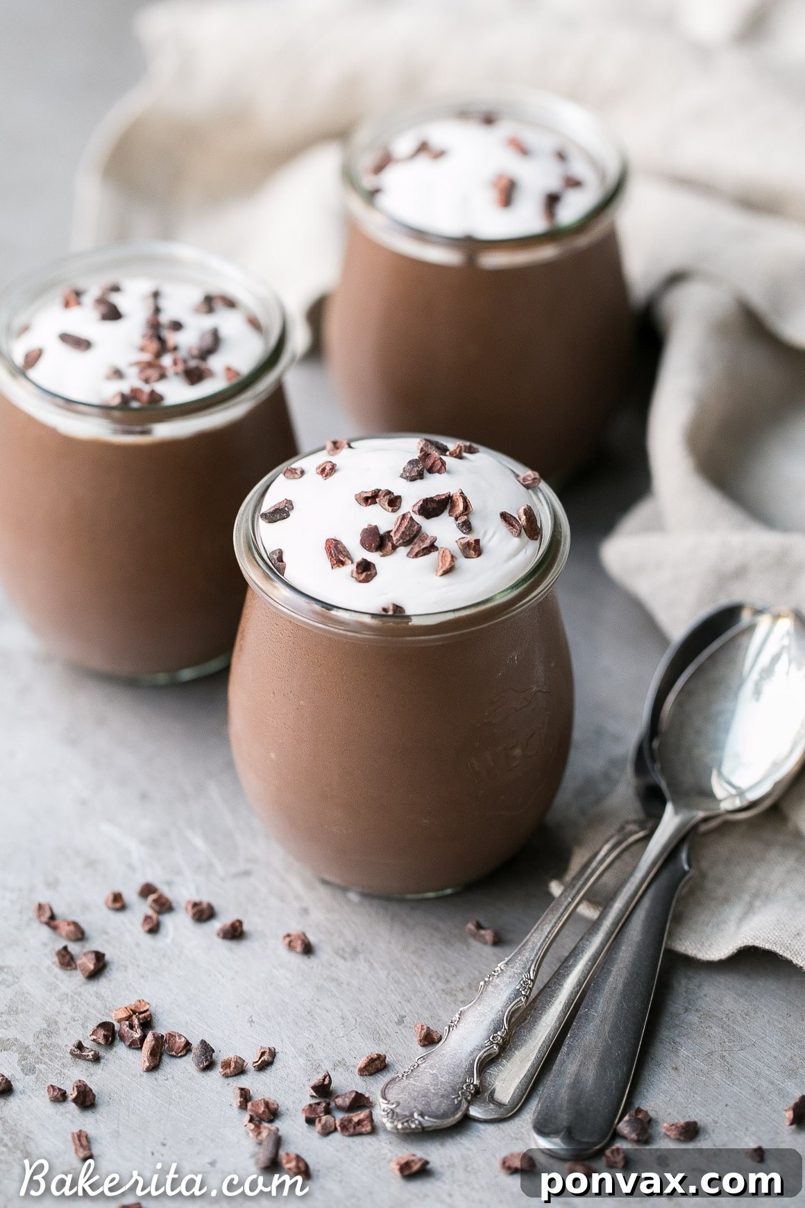 A close-up shot of creamy vegan chocolate pudding served in a glass cup, topped with white coconut whipped cream and chocolate shavings.