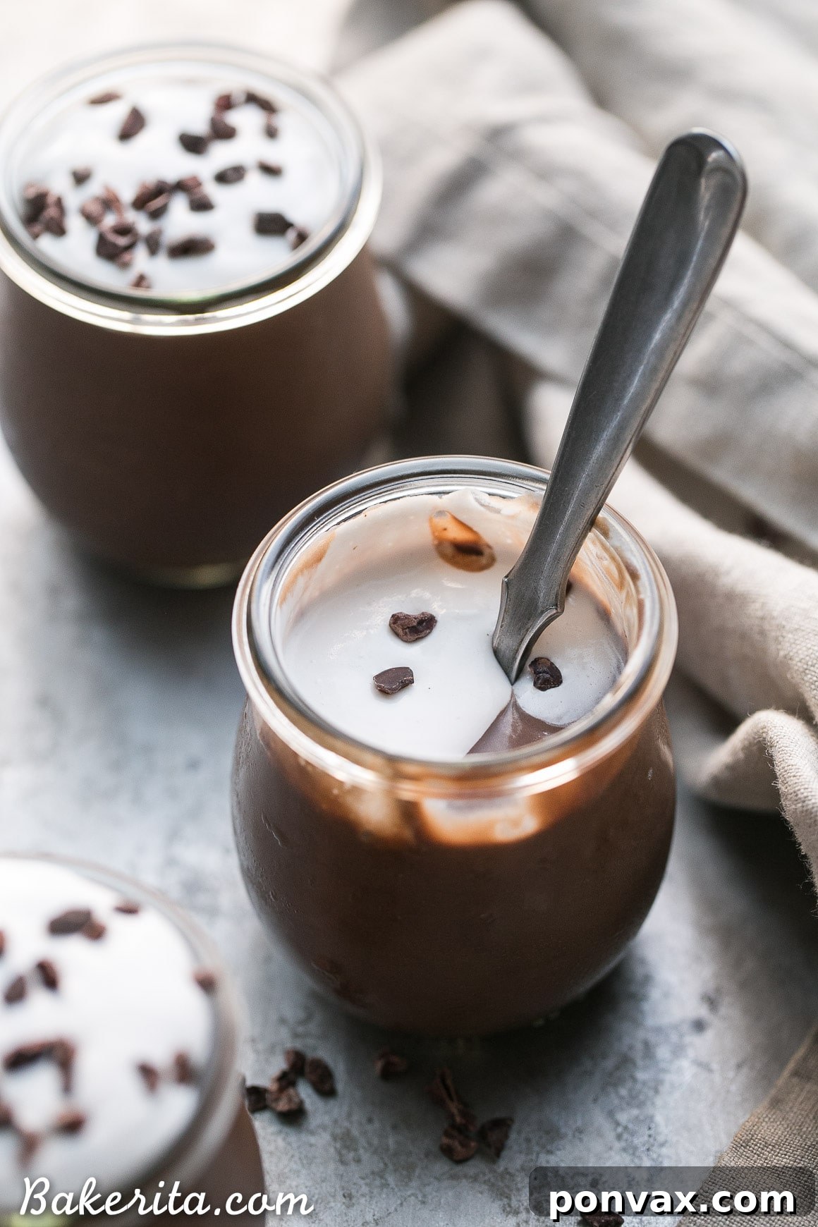 Overhead shot of two bowls of vegan chocolate pudding, one topped with coconut whipped cream and chocolate shavings, the other plain.