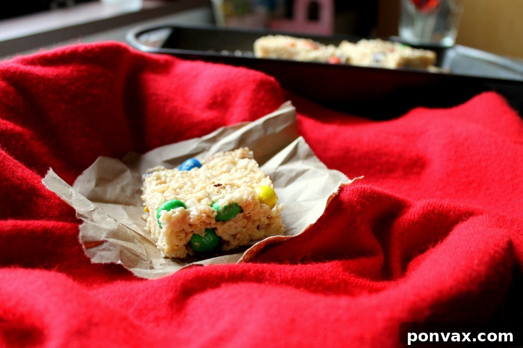 Easy Peanut Butter M&M Rice Krispie Treats Delicious squares of Peanut Butter M&M Rice Krispie Treats, adorned with colorful candies, arranged neatly on a white plate, ready to be enjoyed.