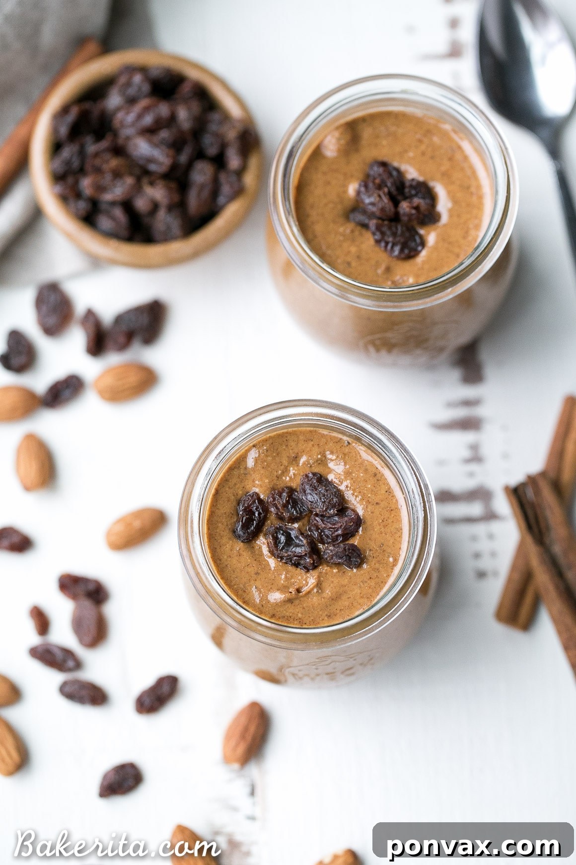A jar of homemade Cinnamon Raisin Almond Butter next to fresh ingredients.