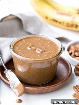 A jar of homemade Banana Bread Pecan Almond Butter with slices of banana and a sprinkle of cinnamon, ready to be enjoyed.