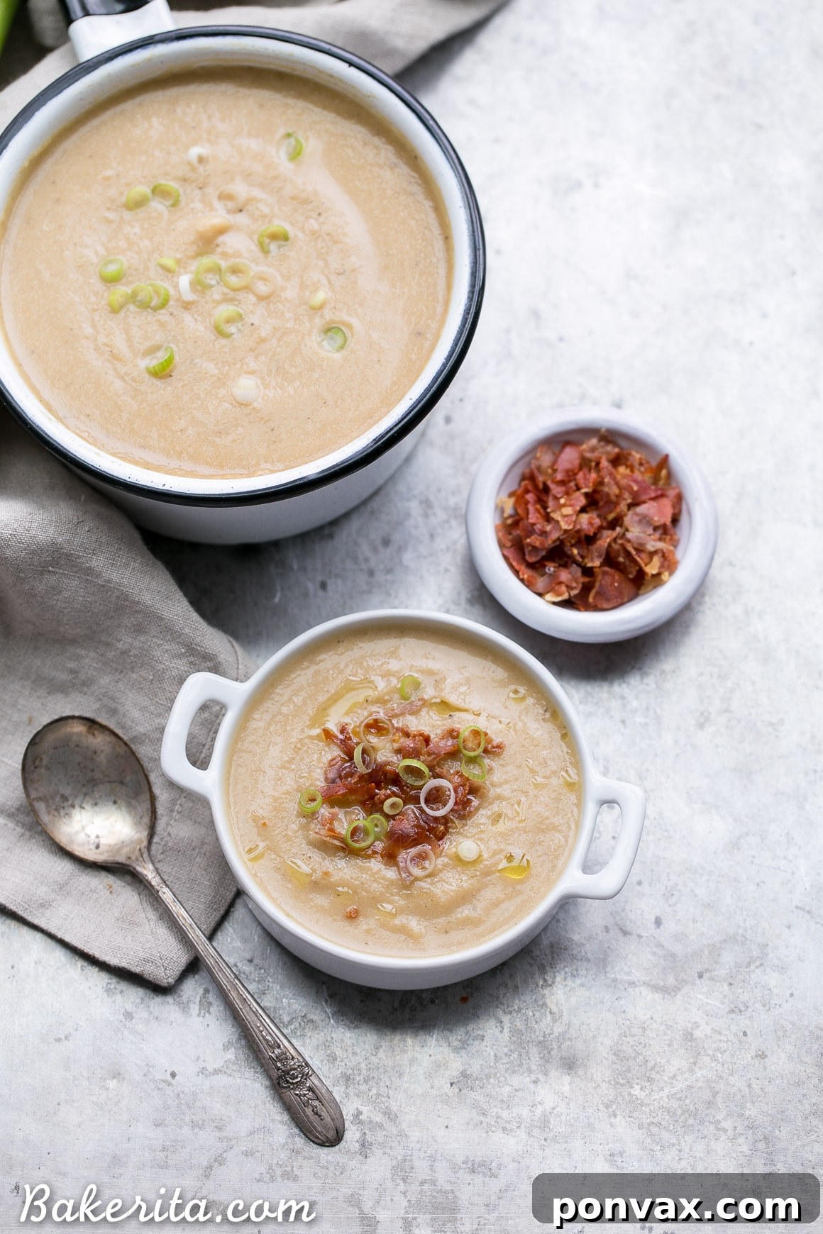 Close-up of a spoon scooping creamy Cauliflower Leek Soup from a white bowl.