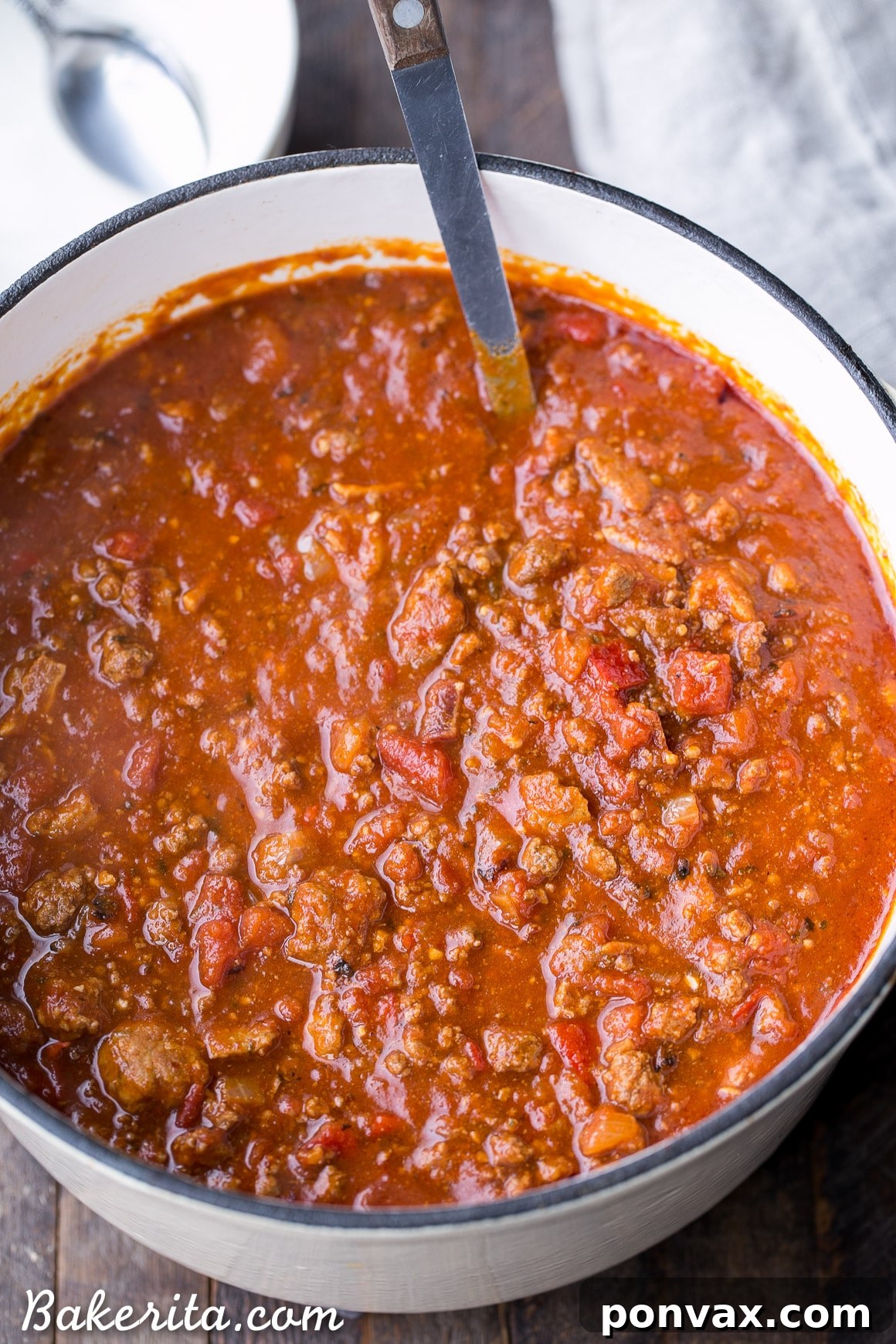 A close-up shot of the raw ingredients for Paleo Chili, including ground beef, Italian sausage, strips of bacon, diced tomatoes, bell peppers, onions, and various spices arranged neatly on a wooden board.