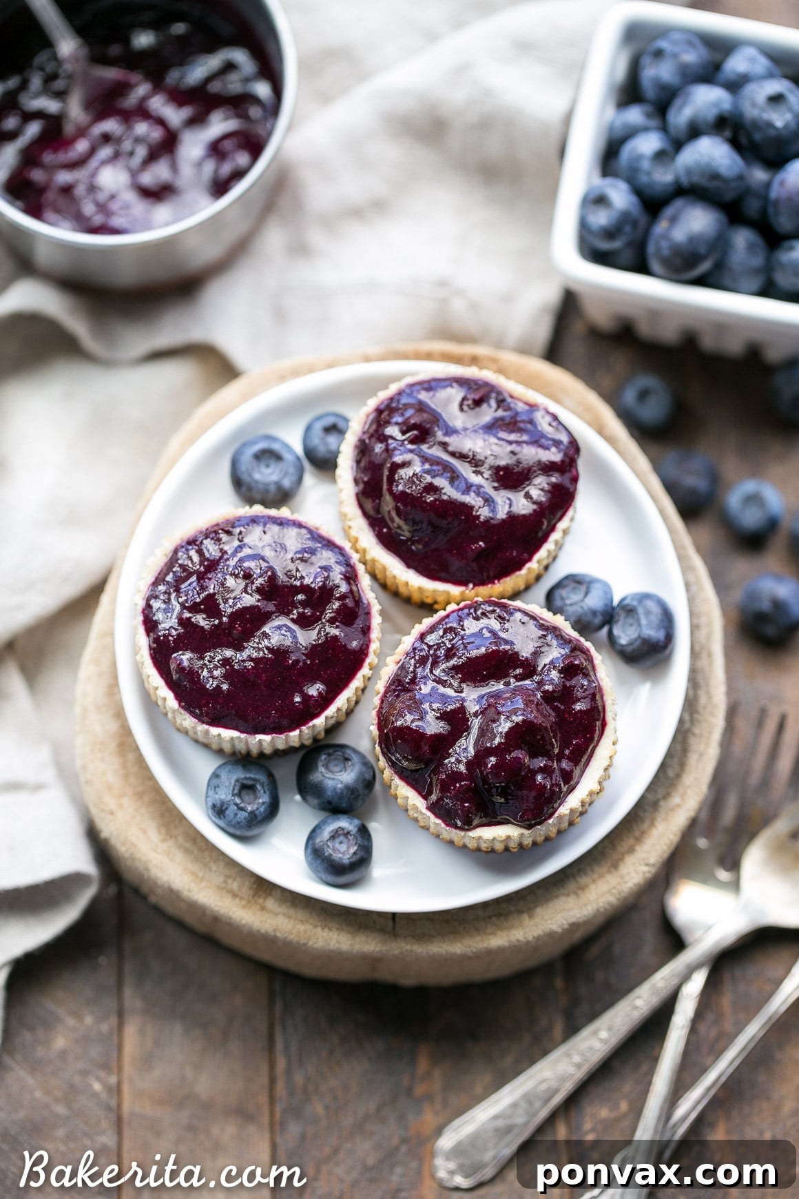A top-down view of several mini Vanilla Bean Greek Yogurt Cheesecakes, each perfectly portioned and ready for a blueberry compote topping, highlighting their smooth, pale filling.