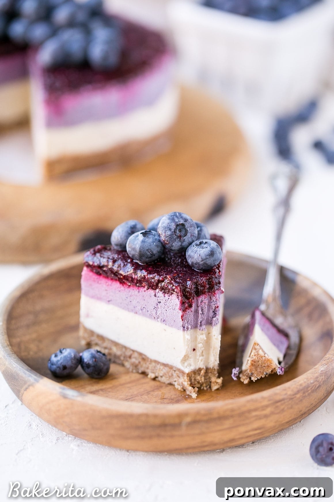 A stunning side shot of the fully assembled no-bake layered blueberry vegan cheesecake, showing all three layers and fresh blueberry garnish, ready to be served.