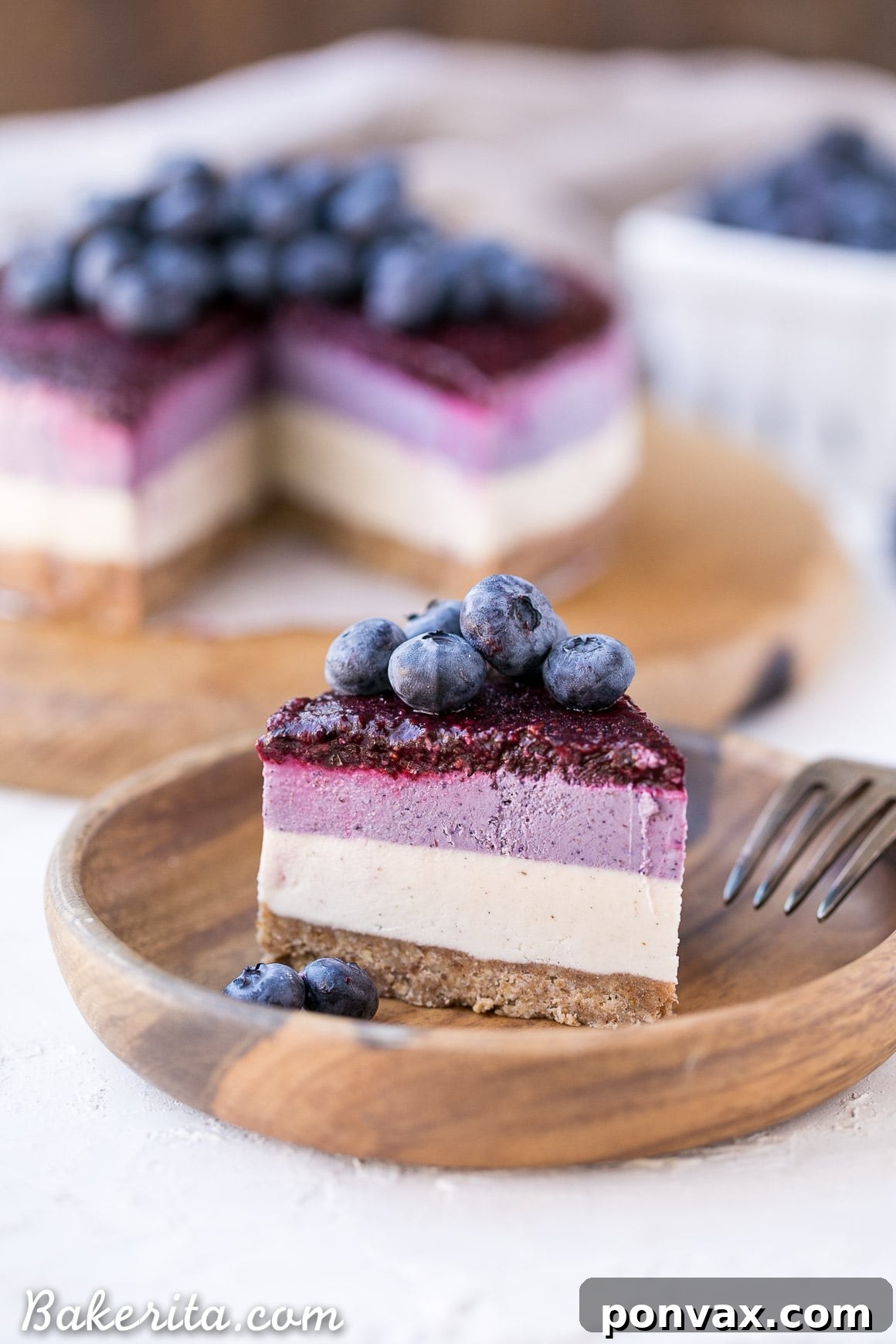 Two whole no-bake layered blueberry vegan cheesecakes on a marble surface, adorned with fresh blueberries and mint leaves, showcasing the vibrant colors.