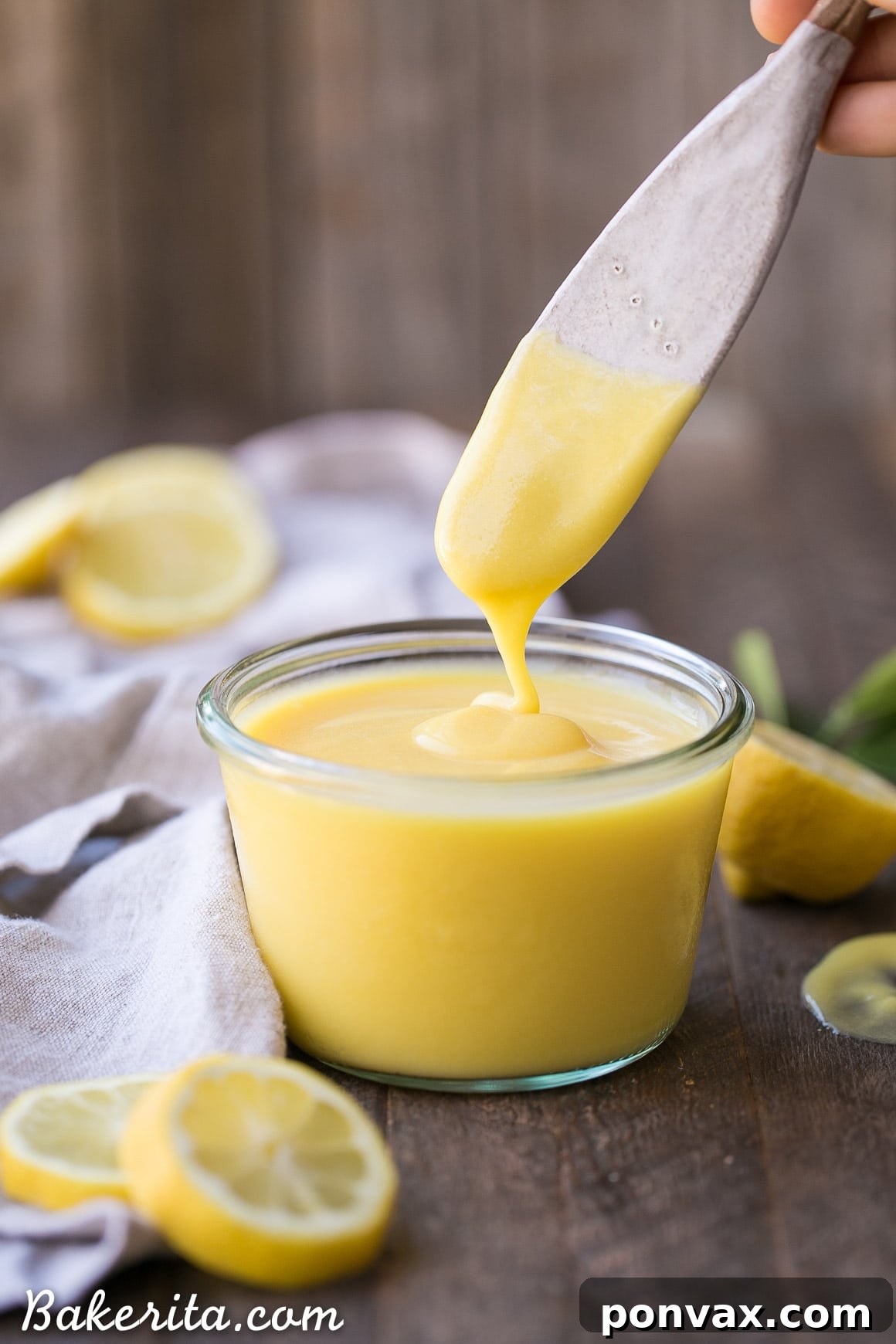 A close-up of a bowl of freshly made Paleo Lemon Curd, drizzled with more curd and garnished with a lemon slice.