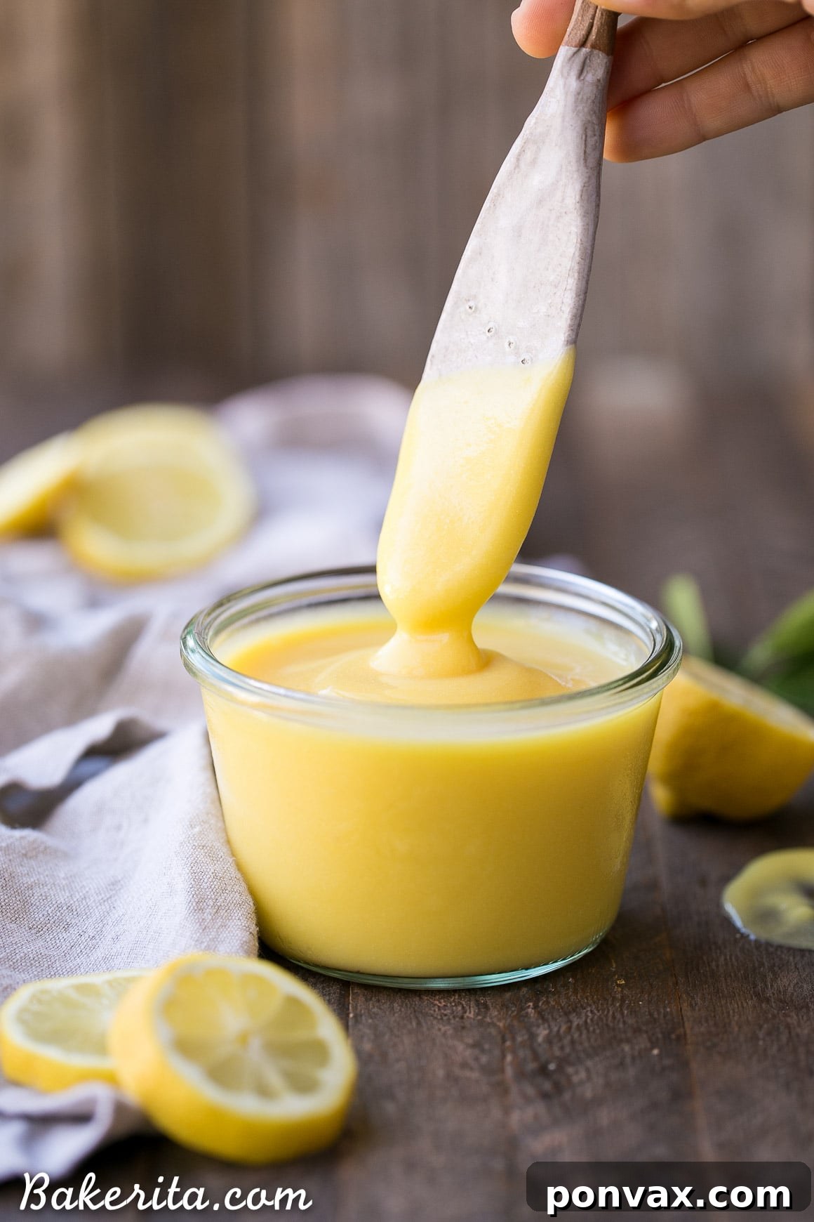 A spoon emerging from a glass jar filled with luscious, bright yellow Paleo Lemon Curd, highlighting its smooth, inviting texture and vibrant color.