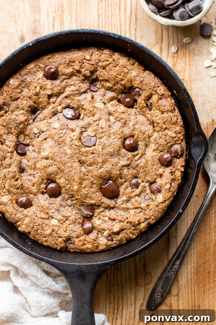Gluten-Free Oatmeal Chocolate Chip Skillet Delight 3 Close-up of a warm, golden-brown Gluten-Free Vegan Oatmeal Chocolate Chip Skillet Cookie in a cast iron pan, showcasing its thick, chewy texture and melted chocolate.