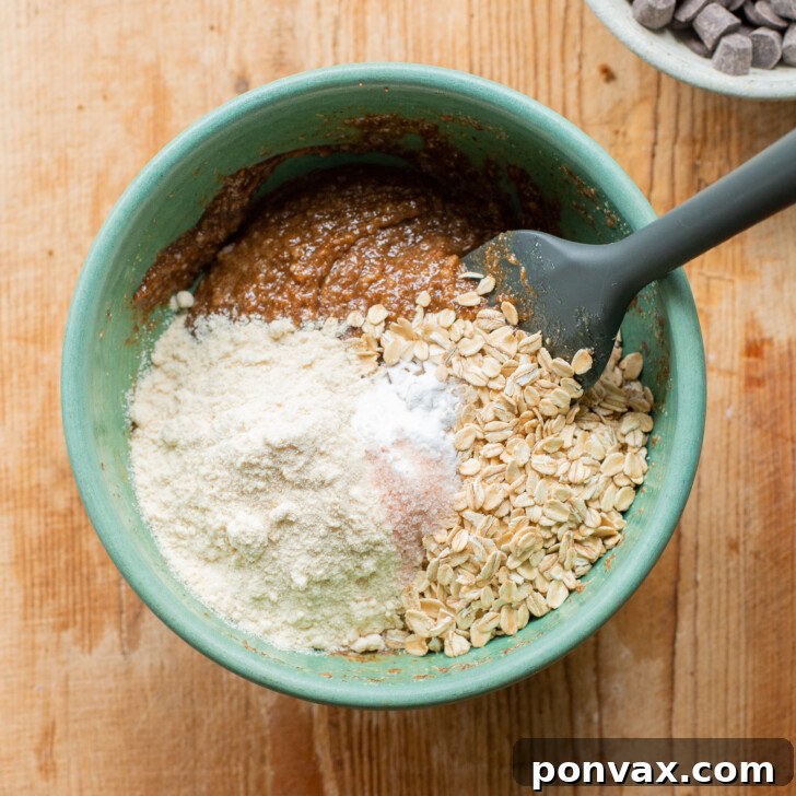 Gluten-Free Oatmeal Chocolate Chip Skillet Delight 10 Image showing dry ingredients (baking soda, salt, coconut flour, rolled oats) being added to the wet mixture.