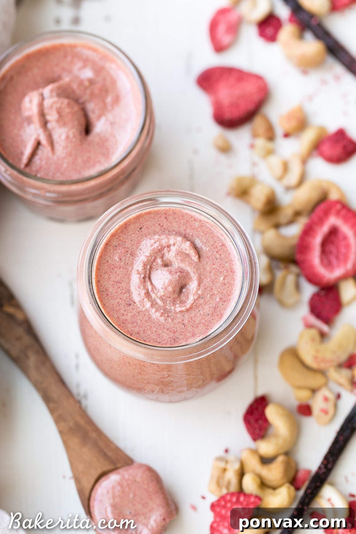 Close-up of a spoon scooping creamy Strawberry Cashew Butter from a jar, showing its smooth texture and flecks of vanilla bean and strawberry.