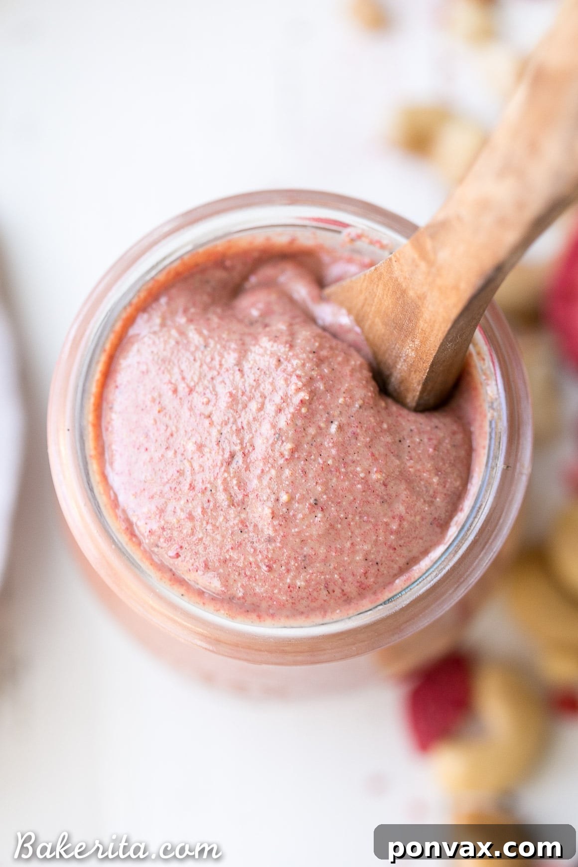 A jar of homemade Strawberry Cashew Butter on a wooden surface, with a spoon resting in it, ready to be enjoyed.