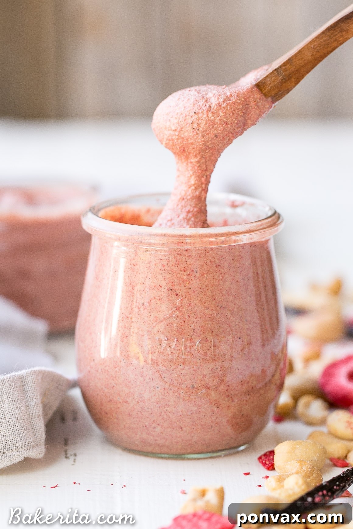 A jar of homemade Strawberry Cashew Butter with a wooden spoon, set against a light background.