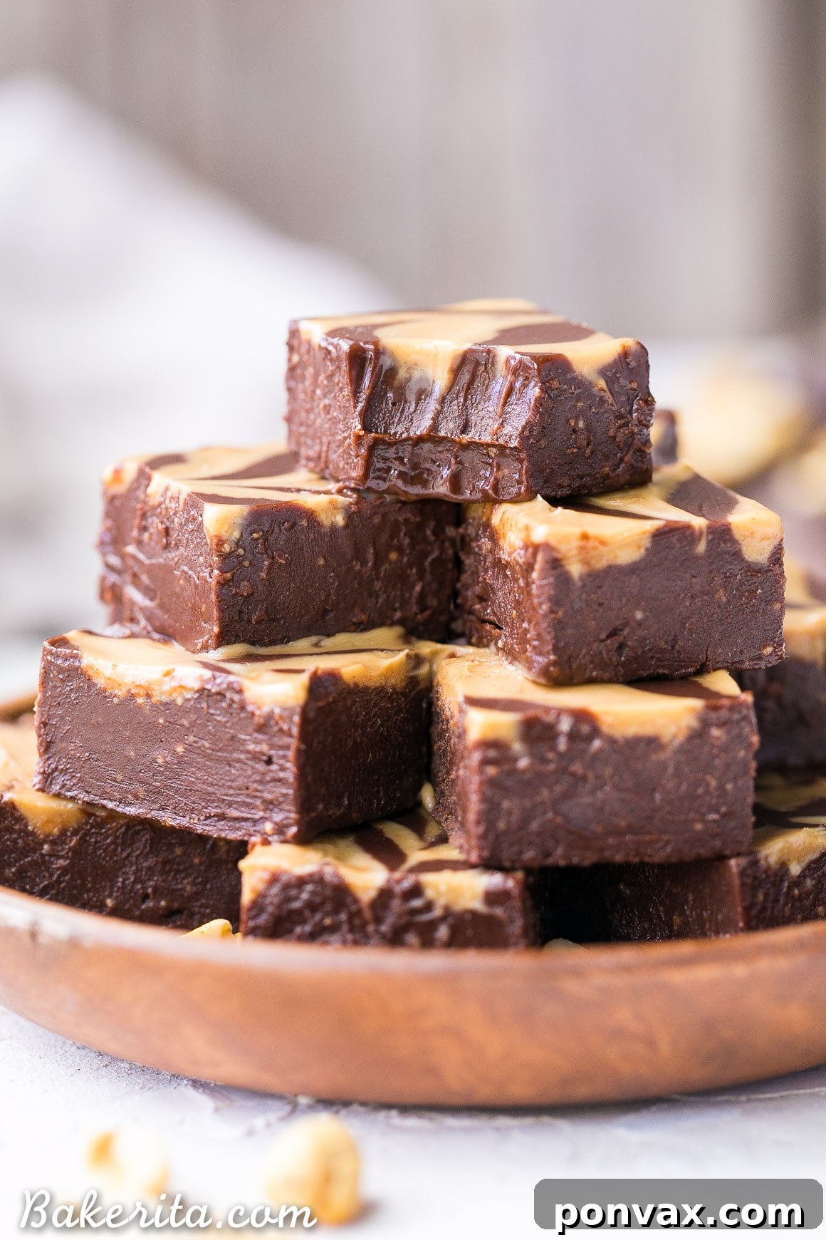 A stack of rich vegan chocolate peanut butter fudge squares, with a beautiful peanut butter swirl on top. The topmost piece has a delightful bite taken out, revealing its creamy texture.