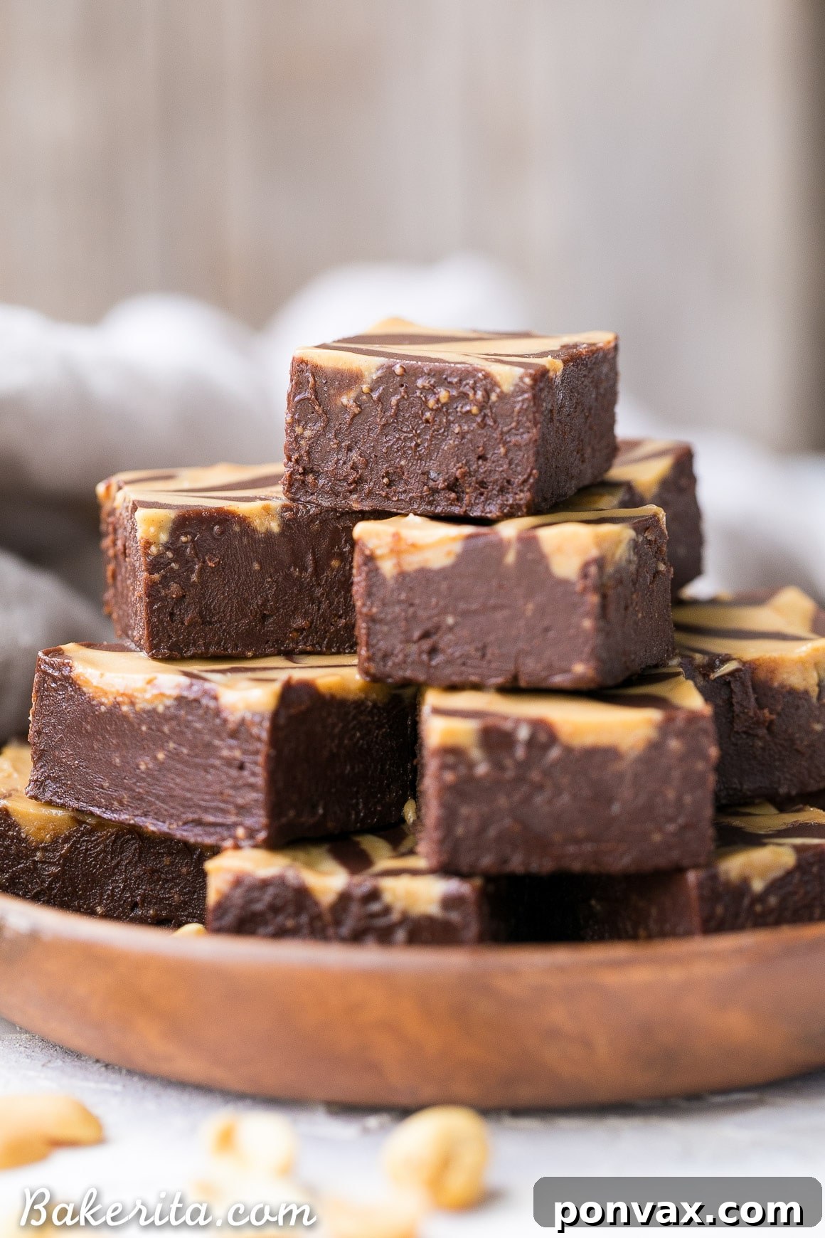 A stack of smooth vegan peanut butter fudge squares, showcasing their rich texture, elegantly arranged on a rustic wooden plate.